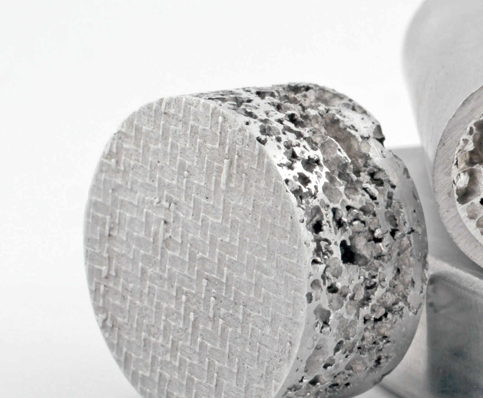 Close-up of a round foam sample: in its end face a fine woven wire mesh lies directly beneath the surface, and the open pore structure is visible on the lateral surface beside it.