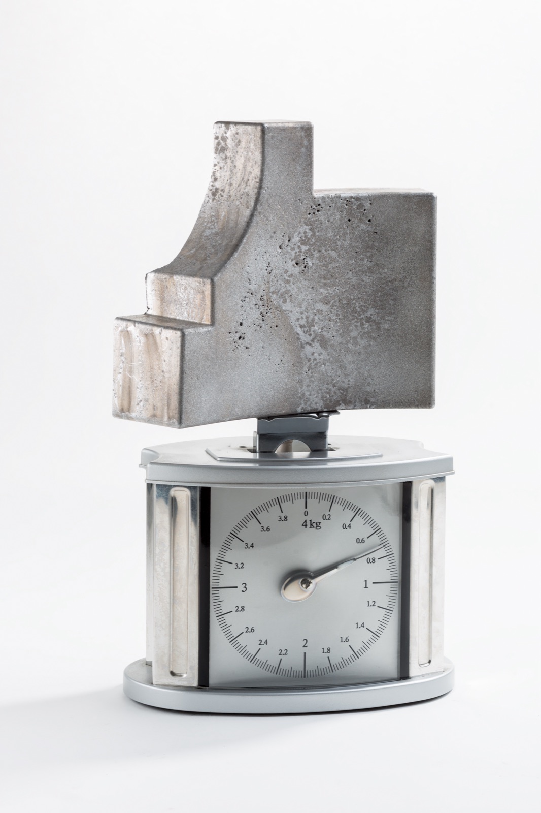 A large shaped element of aluminum foam stands on a mechanical kitchen scale; the needle is well below one kilogram.