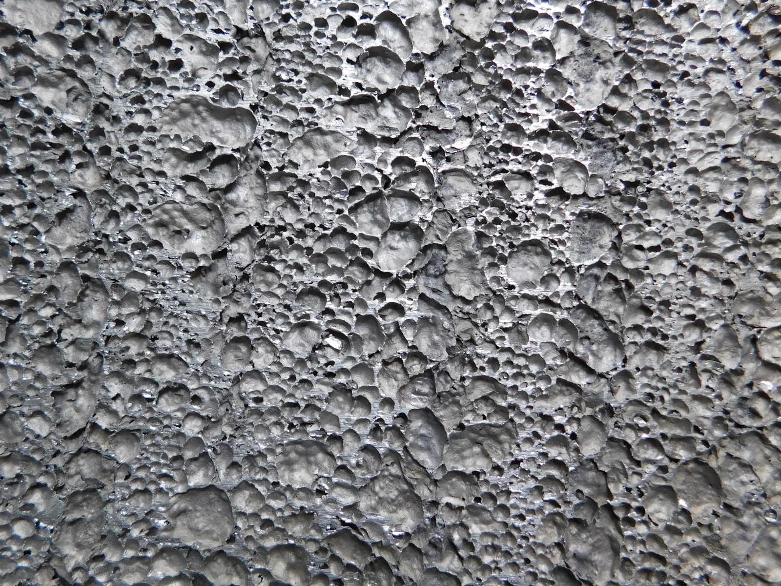 Full-frame close-up of a cut aluminum foam surface: closely packed pores of different sizes with shiny metallic walls between them.