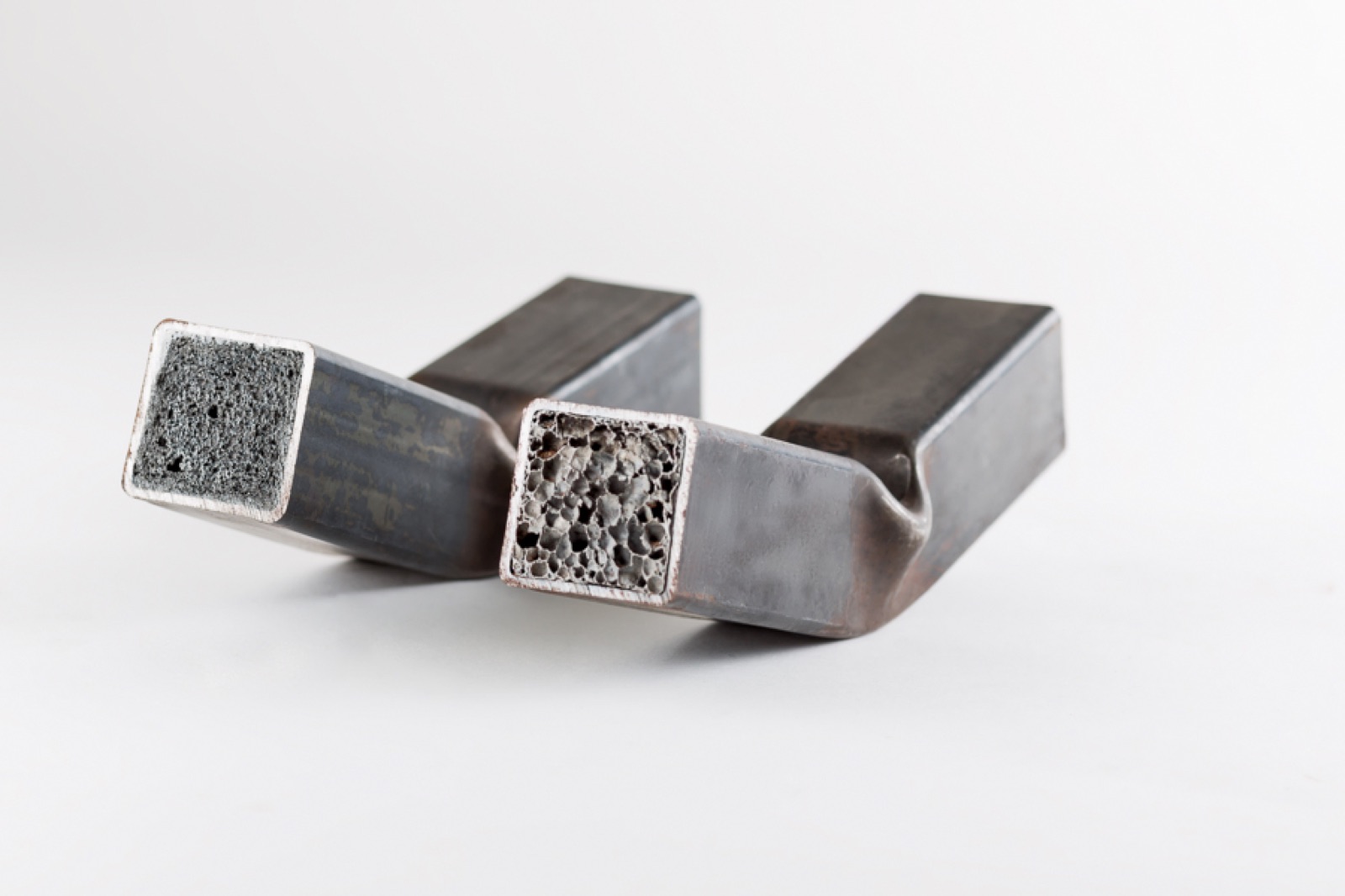 Two foamed square tubes, both folded along their length; at the cut ends the foam core can be seen in cross-section, one fine-pored, the other coarse-pored.