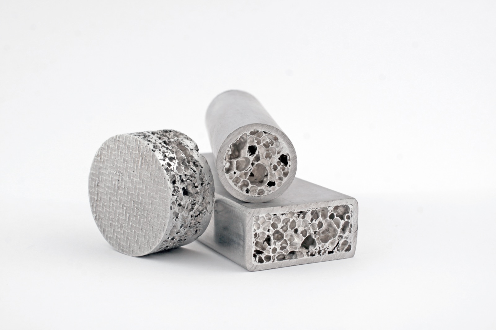 Three foamed profile sections side by side: a round bar and a rectangular profile, both cut open, and a round disc with a woven surface. Every cut face shows the foam core.