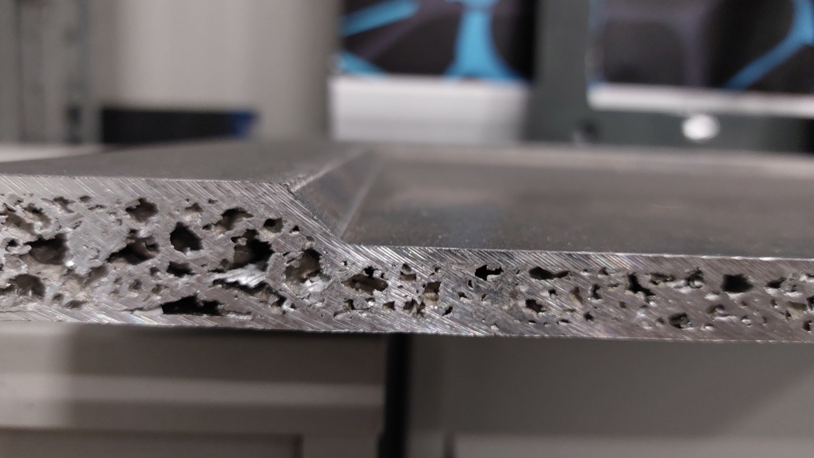 Close-up of the edge of a base plate: the aluminum foam core is exposed at the machined cut face, and the edge is chamfered, tapering to a thinner edge zone.