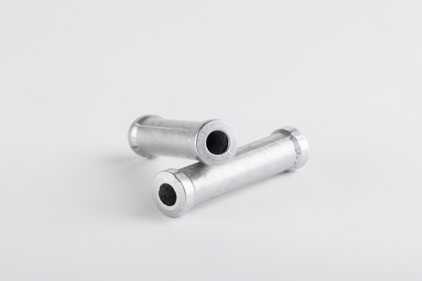 Two small cylindrical components of aluminum; the dark aluminum foam core can be seen at the open end faces.