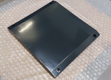 Dark painted, slightly curved component with holes in the corners, lying on bubble wrap.