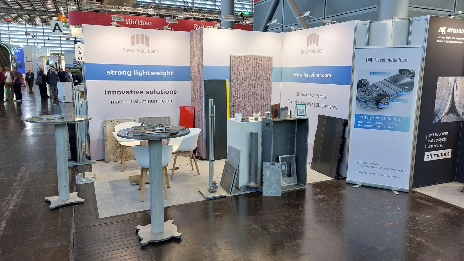 Havel metal foam booth: standing tables, panels and an open housing made of aluminum foam in front of white walls with a blue band.
