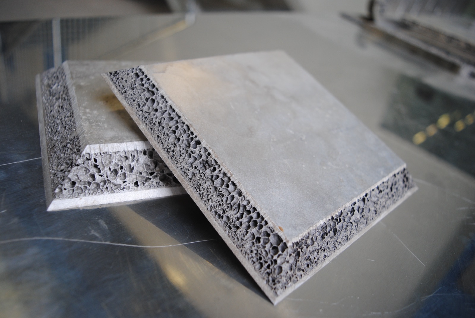 Two sandwich panels stacked on a workbench, both with chamfered edges; at the chamfers the aluminum foam core lies exposed between the cover layers.