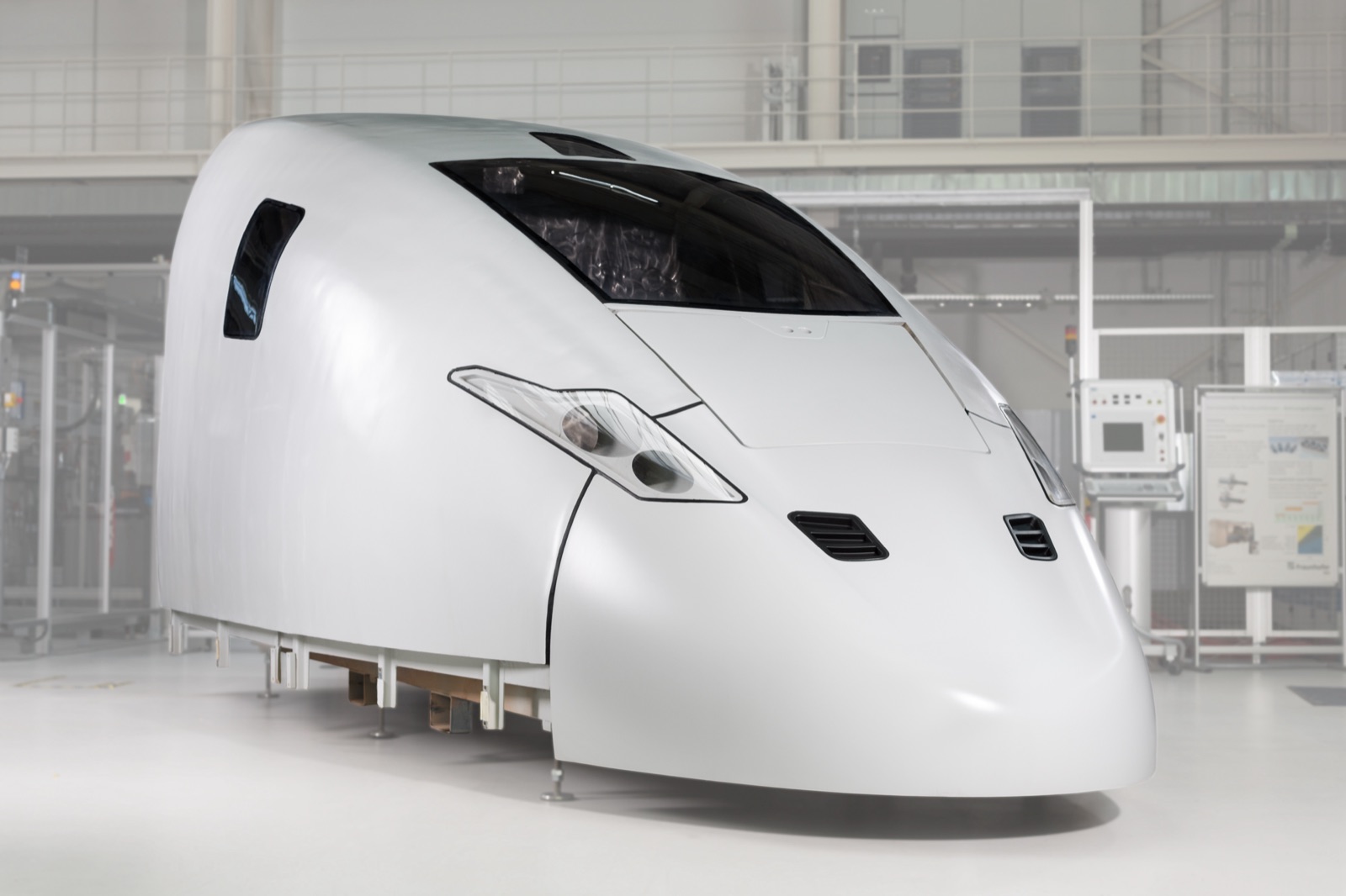 The finished, white-painted power car hood of an express train stands in a hall: a continuously curved front with a fitted windscreen, side windows and ventilation grilles.