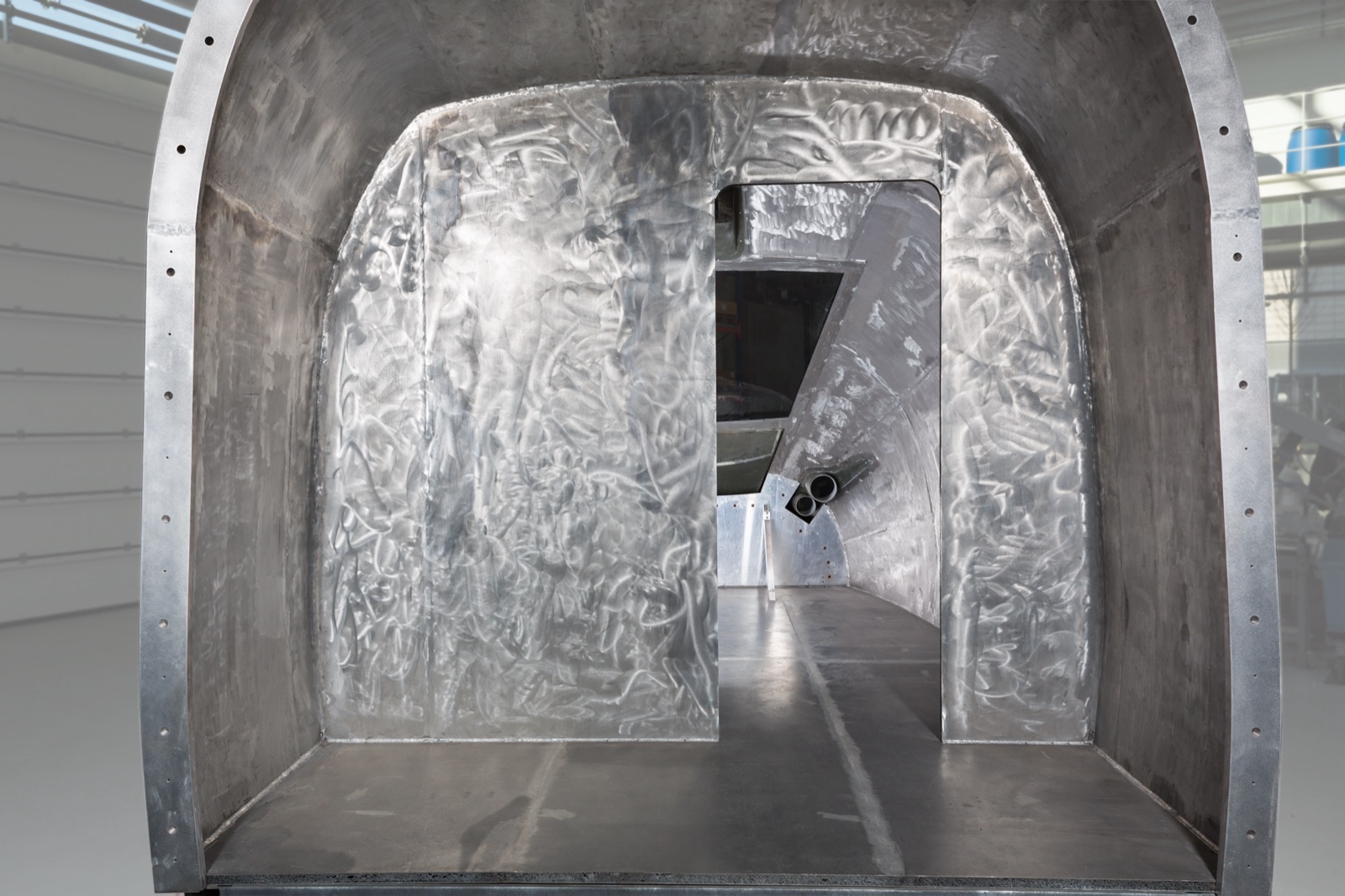 View from behind into a large, barrel-vaulted structure of aluminum sandwich panels: the power car hood of an express train, with a passage through the bulkhead, set up in a production hall.
