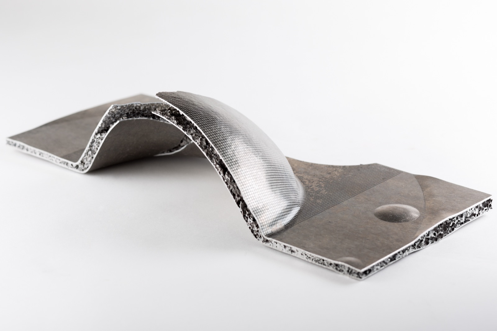 A sandwich specimen formed into a dome, its surface carrying a fine measuring grid. At the edge of the dome the sheet has torn open and the aluminum foam core is exposed.
