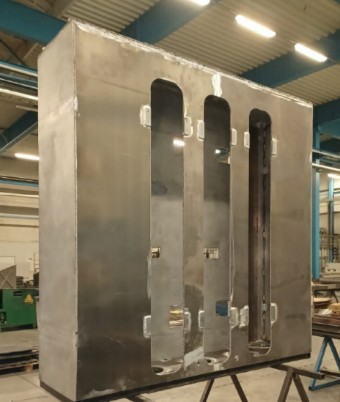 Upright, large frame of sandwich sheets with three vertical cut-outs, in a production hall.